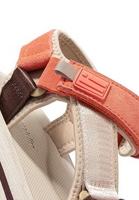 Sandalia ajustable con una correa de ante naranja, base de textil beige y un acento marrón. Cuenta con una hebilla de plástico para un ajuste seguro.