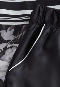 Fekete anyagú szett fekete-fehér csíkos felsővel, amely virágmintákat tartalmaz. A nadrág gumis derékpánttal és fehér szegéllyel rendelkezik.