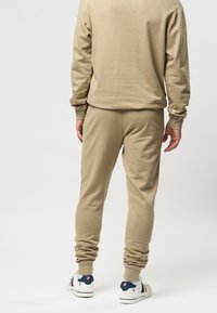 Beige sweatshirt en joggers set gemaakt van zachte stof. Slim-fit ontwerp met ribgebreide manchetten. Model draagt witte sneakers met blauwe accenten.