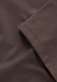 Barna szövet, sima textúrával és behajtott szegéllyel, finom varrással a varrás mentén, és puha, matt felülettel.