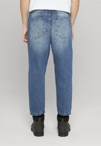 Light blue denim jeans with a relaxed fit, featuring two back pockets and visible stitching. Cuffed hem, worn with black boots.
