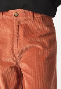 Close-up of burnt orange corduroy pants with a button and zipper fly worn with a black top.