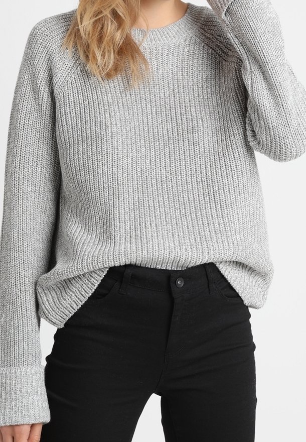 Personne portant un pull en maille gris clair légèrement rentré dans un pantalon noir taille haute avec fermeture par bouton.