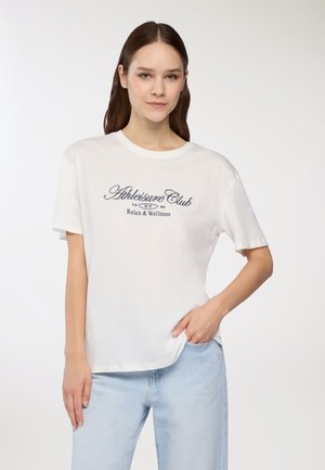 T-shirt bianco in cotone con maniche corte, scollatura rotonda e testo stampato blu navy che dice "Athleisure Club Relax & Wellness." Vestibilità casual.