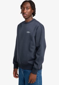 Felpa blu navy con collo a giro, polsini e bordo a costine. Presenta un piccolo logo bianco sul petto. Realizzata in un tessuto morbido e texturizzato.