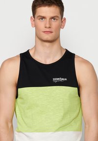 Juodas ir žalias dryžuotas marškinėlis su balta apatine dalimi. Yra apvalus kaklas ir "KORÖSHI engineered" logotipas ant krūtinės.