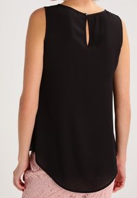 Top sans manches noir en tissu lisse, présentant un dos en découpe clé avec fermeture à bouton et un ourlet courbé, associé à une jupe en dentelle.