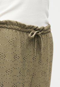 Βαμβακερή φούστα με κεντήματα floral με τρυπητό σχέδιο, ελαστική μέση και δεμένη κορδονέτα, φορεμένη με λευκό τοπ σε ουδέτερο φόντο.