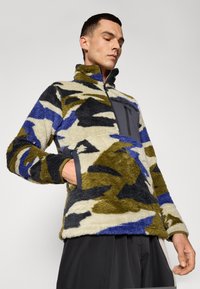 Fleece-Pullover im Tarnmuster, mit blauen, grünen und schwarzen Akzenten, hohem Kragen, Reißverschluss-Brusttasche und Seitentaschen.