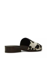 Mule à enfiler avec petit talon bloc en bois, empeigne imprimé vache noir et blanc, et clous argentés le long de la base.