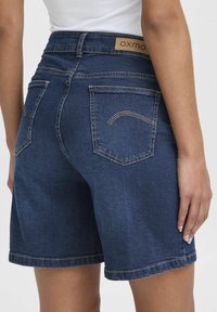 Denimshorts i mörkblått med hög midja, med två bakfickor, kontrasterande sömmar och upplagt fåll. Bromärken synliga.