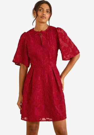 Rotes Spitzenkleid mit kurzen Puffärmeln, einem Schlitzkragen, tailliertem Schnitt und ausgestelltem Rock. Durchgängiges strukturiertes Blumenmuster.