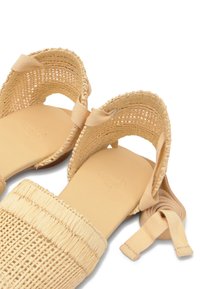 Sandales tissées beige avec talons ouverts, brides de cheville et larges bandes texturées aux orteils, conçues pour un usage décontracté.
