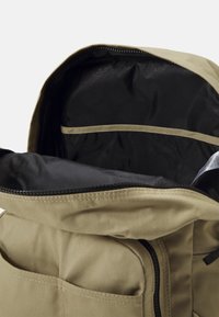 Tamsiai žalia kuprinė su lankstomu užtrauktuku, juoda vidaus pamušalu, užtrauktuko uždarymu ir šoniniu kišeniu. Medžiaga atrodo patvari su lygia tekstūra.