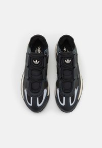 Para czarnych i szarych sneakersów Adidas z białymi i siateczkowymi detalami, widziana z góry na białym tle.