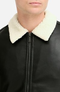 Jachetă din piele neagră cu guler din blană crem, având un închizător frontal cu fermoar și suprafață texturată. Prim-plan al gulerului și părții superioare a corpului.