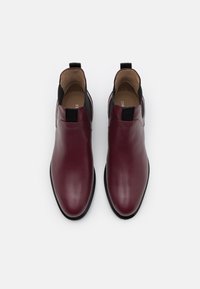 Botines de cuero burdeos con paneles laterales elásticos negros, puntera redondeada y suela texturizada. Diseño minimalista sin hardware visible.