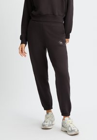 Pantalones de chándal negros con puños elásticos y un sutil detalle de logo en el lateral. Están hechos de una tela suave y presentan un corte relajado para mayor comodidad.