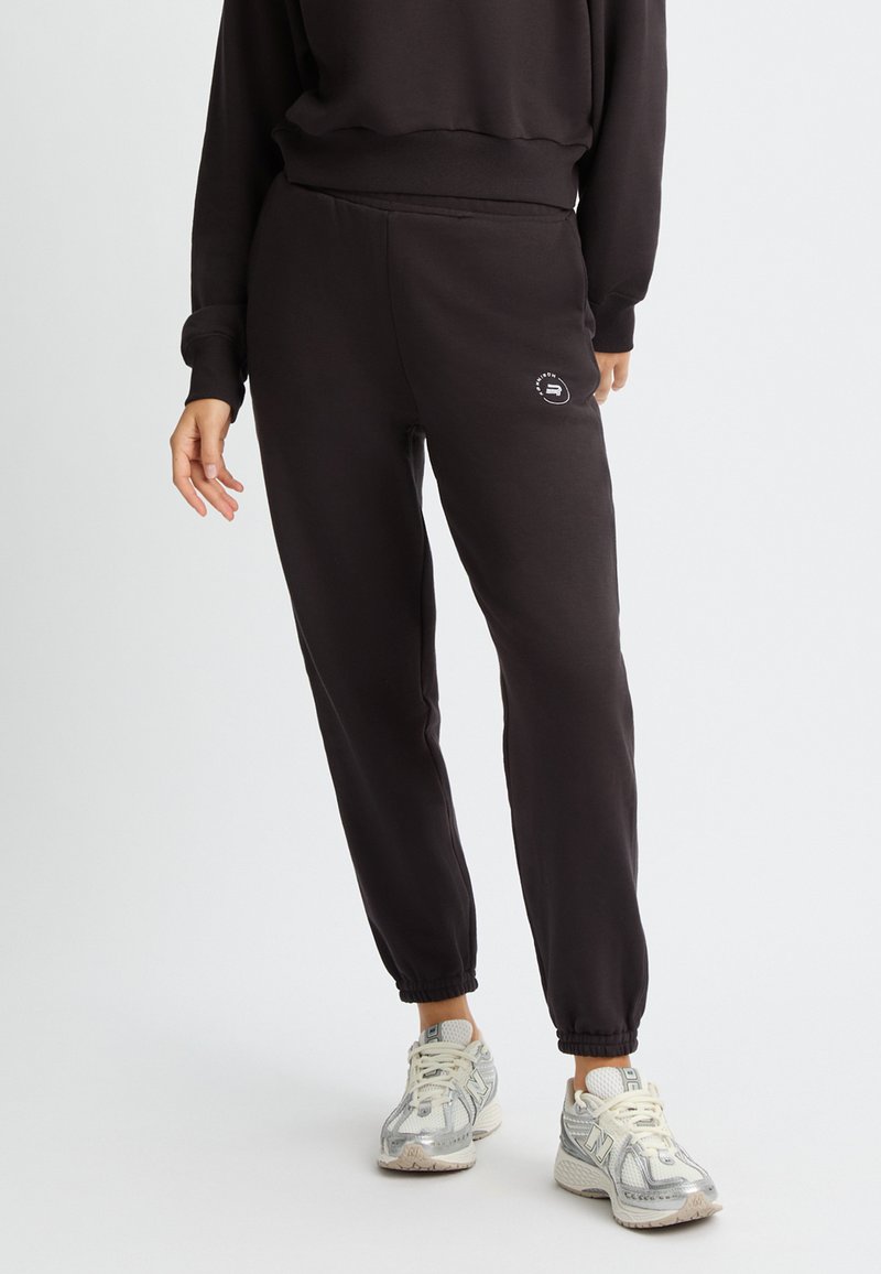 Pantalones de chándal negros con puños elásticos y un sutil detalle de logo en el lateral. Están hechos de una tela suave y presentan un corte relajado para mayor comodidad.