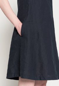 Robe en lin bleu marine avec un design évasé et des poches sur les côtés. Présente une texture lisse et un ourlet qui tombe au-dessus du genou.