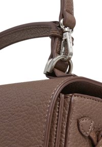 Brūns teksturēts ādas somas siksna, kas piestiprināta pie sudraba metāla sprādzes, ar smalku dūrienu detaļu somas malā un vāka daļā.