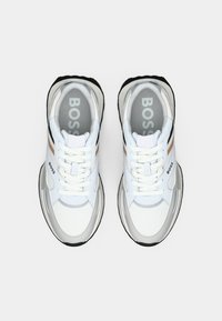 Zapatillas de material mixto con una base blanca, acentos grises y suelas de goma negras. Los cordones y la marca son visibles en la parte superior.