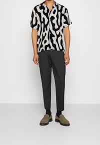 Camicia a maniche corte in un motivo astratto bianco e nero, abbinata a pantaloni scuri e mocassini oliva, con una vestibilità comoda e un tessuto leggero.