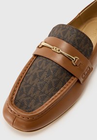 Smeđi kožni loafers s smešnim uzorkom na tkanini, sa zlatnim akcentom i detaljnim šavom duž spoja.
