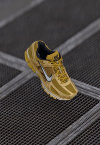 Baskets de course Nike jaunes avec tige en mesh, intérieur noir et logo swoosh blanc. Présente une semelle texturée et un système de laçage pour un maintien sécurisé.