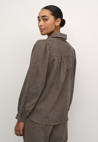 Brown textured long-sleeve shirt with a collar, puffed shoulders, and buttoned cuffs, featuring a yoke seam and relaxed fit.