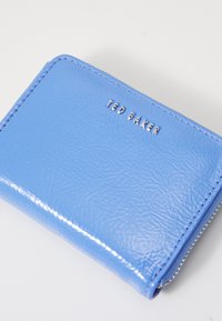 Portafoglio blu in pelle con finitura strutturata, dotato del logo argentato "TED BAKER" sulla parte anteriore e di una chiusura a zip lungo il lato.