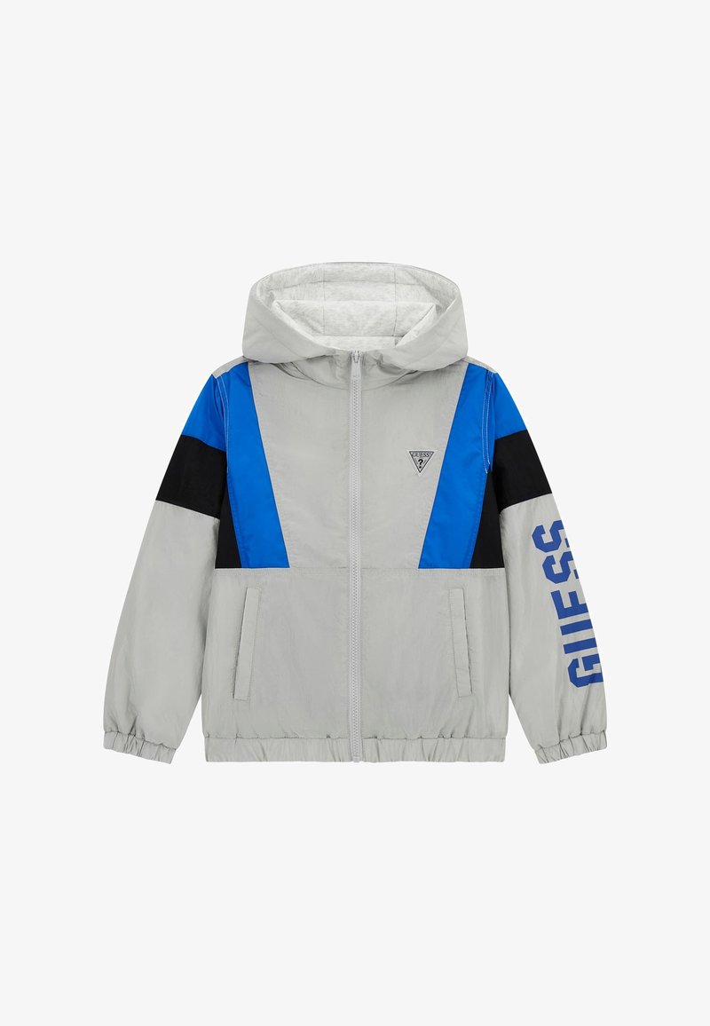 Helehall hall jacket sinise ja musta aktsendiga, tõmblukuga, elastsete varrukatega ja "GUESS" brändimisega sinisel varrukal.