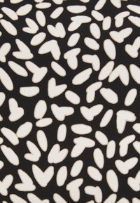 Mustan kankaan pinnalla on abstrakti kuvio, jossa valkoiset muodot muistuttavat pieniä sydämiä. Kankaalla on sileä rakenne ja hienovaraiset ompelu yksityiskohdat.