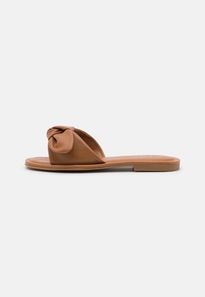Flad slidesandal i tan-farvet læder med et knudet design foran, glat tekstur og en minimalistisk sål i kork.