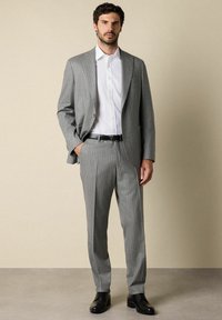 Grijze streepjessuit met een getailleerde pasvorm, stofstructuur goed zichtbaar. Gecombineerd met een witte button-up overhemd en zwarte leren schoenen.