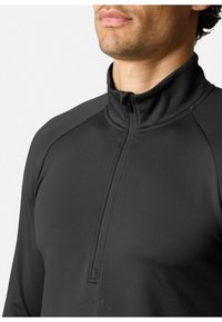 Pullover nero con mezza zip realizzato in tessuto elastico con una texture liscia, con colletto alto e maniche raglan. Dettaglio logo discreto sul petto.