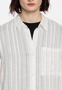Button-up shirt made of lightweight fabric with vertical gray and white stripes. Features a chest pocket and a classic collar.