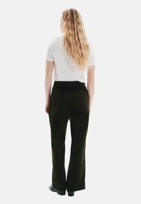 Pantalons en velours côtelé verts à taille haute, avec des jambes évasées et des poches arrière, associés à un haut blanc ajusté à manches courtes.