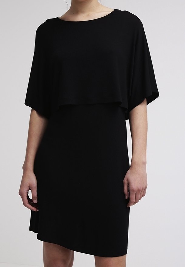 Černé šaty s volnou, zavěšenou vrstvou a přiléhavou spodní částí. Měkká látka, kulatý výstřih a asymetrický detail spodního lemu.