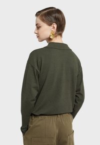 Maslinasto zeleni pulover s ovratnikom, širokog kroja i dugim rukavima, uparen s bež vojnim hlačama s bočnim džepovima.