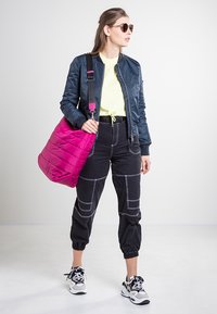 Granatowa kurtka bomberka, neonowo-żółta koszulka, czarne spodnie cargo z białymi przeszyciami, różowa pikowana torebka na ramię oraz sportowe buty.