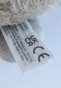 Close-up of a plush toy’s fabric label showing UKCA and CE safety marks, with manufacturing and quality control details.