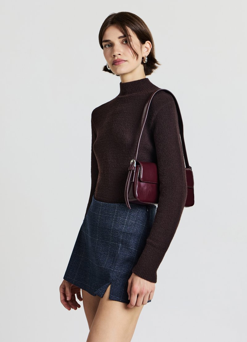 Brauner Strickpullover mit hohem Kragen, blau karierter Minirock mit Frontrissen und eine burgunderrote Leder-Umhängetasche mit silberner Schnalle.