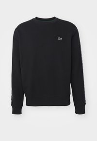 Sweat-shirt noir à col rond, manches longues et ourlet ajusté. Il présente un petit logo Lacoste vert sur la poitrine et des accents de bande latérale.