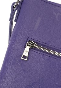 Borsa a tracolla in pelle viola con texture, dotata di logo impresso, chiusura con zip argentata e un dettaglio nella linguetta della zip.