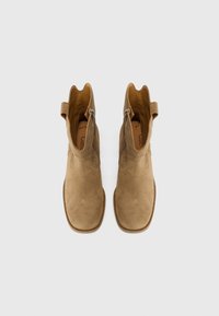 Stivaletti alla caviglia in suede beige con una texture liscia, tagli curvi nella parte superiore e cerniere laterali. I bordi cuciti rinforzati aumentano la durata.