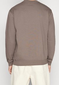 Sweatshirt en coton marron avec manches longues, col rond et ourlet à côtes, présenté de dos. Texture douce et design simple.