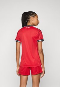 Röd idrottströja och shorts i ett mjukt material. Tröjan har ärmar och krage med svart kant. Korta ärmar och avslappnad passform.