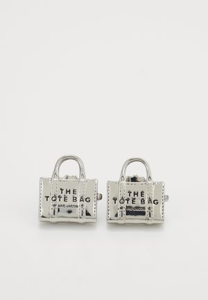 Gemelli da polso color argento progettati come miniature di borse tote, con testo inciso e manici, che riflettono una superficie metallica lucida.