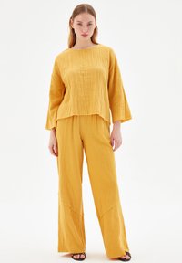 Geel, textuur, twee-delige outfit met een losse top met lange mouwen en wijde broek, beide met een casual, ontspannen silhouet.